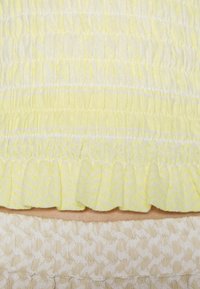 Tecido amarelo texturizado com riscas horizontais e uma bainha franzida, sobreposto a um tecido bege com um padrão subtil.