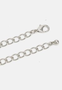 Chaîne en métal argenté avec des maillons ovales, un fermoir homard à une extrémité et une petite perle ronde à l'autre, sur fond blanc.