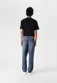Tricou negru cu mânecă scurtă, pantaloni din denim albastru lejer, cu două buzunare la spate, și adidași albi. Pachet din piele pe talie.