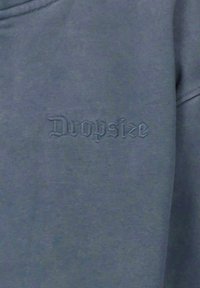 Sivi dukserica s tonalno vezanim logotipom "Dropsize". Mekana tekstura, opušteni kroj i jednostavan izrez oko vrata.