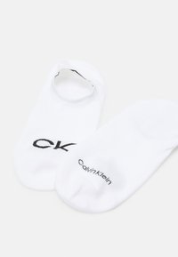 Balti blauzdų kojinaitės, pagamintos iš medvilnės mišinio, su juodu "CK" logotipu viršuje ir "Calvin Klein" tekstu šone. Lygus paviršius, minimalus dizainas.