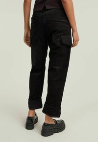 Zwarte corduroy cargo broeken met opgerolde boorden, voorzien van zijzakken en een textuurstof. Gemaakt met chunky zwarte schoenen.