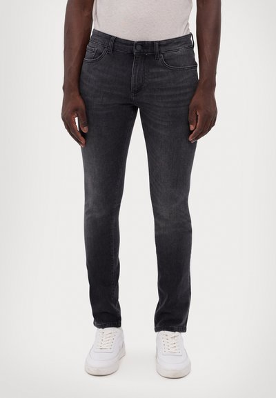 Jeans slim en denim gris foncé, avec un design classique à cinq poches, fermeture à bouton et décoloration subtile pour la texture. Une paire de baskets blanches.