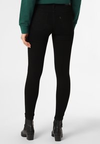 Black skinny jeans made of stretchy denim, featuring a classic five-pocket design, seamless back, and contrasting stitching details.