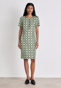 Kurzärmliges Kleid in Hellgrün mit schwarzen geometrischen Mustern. Gerader Schnitt, knielang, mit rundem Ausschnitt und einfachen vorderen Knöpfen.