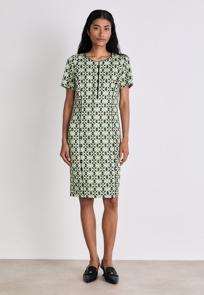 Kurzärmliges Kleid in Hellgrün mit schwarzen geometrischen Mustern. Gerader Schnitt, knielang, mit rundem Ausschnitt und einfachen vorderen Knöpfen.