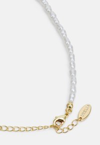Gouden ketting met witte parels, voorzien van een karabijnsluiting en een klein label met de merknaam erin gedrukt.