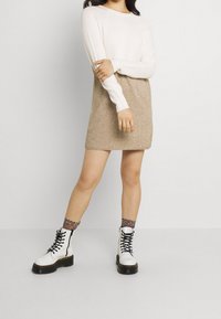 Robe pull tricotée avec des manches longues, haut beige et jupe beige. Assortie à des bottes de combat blanches à lacets et des chaussettes à motifs léopard.