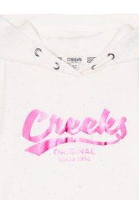 Felpa bianca con spruzzi multicolori, dotata di un logo 'Creeks' rosa lucido e la scritta 'Original Since 1974' in un design curvo.