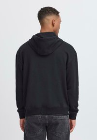 Svart hettegenser laget av mykt stoff, med avslappet passform, ribbede mansjetter og fald, og et enkelt design uten mønstre.