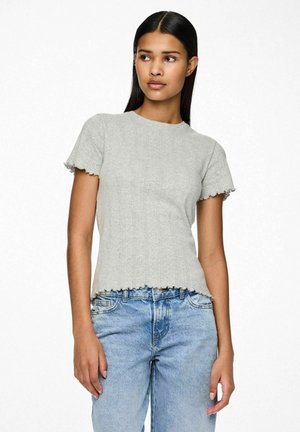 Siva kratka majica s kratkimi rokavi iz rebraste tkanine. Ima okroglo ovratnik in valoviti rob. V kombinaciji s svetlo modrimi kavbojkami.