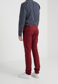 Pantalon en coton rouge slim fit, avec des poches arrière, associé à une chemise à motifs marine et des baskets blanches.