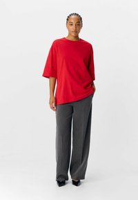 Rød oversized T-shirt lavet af bomuld, parret med grå vide benbukser og sorte spidse sko. Minimalistisk design, afslappet pasform.