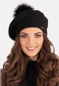 Fekete kötött baret sapka texturált felülettel és bolyhos pom-pommal a tetején. Oldalán egy kis fémtűzött logó díszítés található.