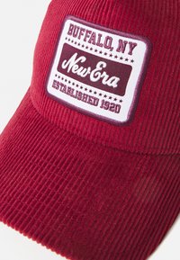 Rød kordfløjlskasket med en hvid rektangulær lap, der har teksten "Buffalo, NY" og "New Era", etableret 1920, samt dekorative stjerner.