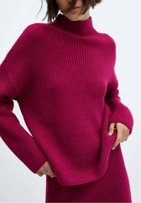 Fuksjowy sweter dzianinowy z prążkowaną fakturą, z wysokim kołnierzem, luźnym krojem, długimi rękawami oraz miękką strukturą, z delikatnym drapowaniem u dołu.