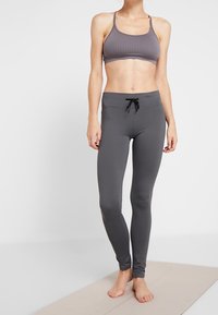 Reggiseno sportivo grigio con texture a coste, abbinato a leggings grigi aderenti con vita regolabile e superficie liscia.