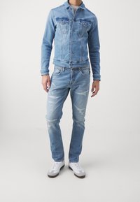 Ljusblå denimjacka med två bröstfickor och slitna ljusblå jeans. Bärs med vita sneakers med grå detaljer.
