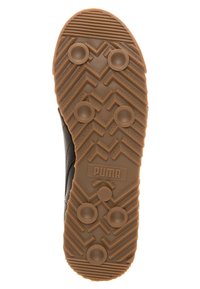 Sula av en brun Puma-sko med cirkulära nitar, zickzackmönster och "PUMA"-logotyp i mitten, designad för grepp och icke-märkande användning.