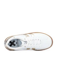 Zapatilla deportiva blanca con detalles dorados, suela de goma, cierre de cordones en la parte delantera y tres rayas contrastantes en el lateral. Material superior texturizado.