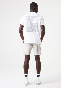 Camiseta blanca de algodón con un gráfico de línea negra en la parte posterior, combinada con pantalones cortos a rayas beige, calcetines blancos y zapatillas blancas.