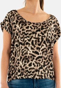 Top de manga corta con estampado de leopardo en beige y negro, con un escote amplio, textura de tela suave y un corte holgado. Combinado con jeans de mezclilla.