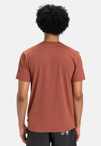 Short-sleeve, crew-neck t-shirt in rusty red fabric, with a smooth texture. Features a simple design and no visible patterns or accents.