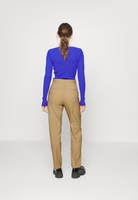 Beżowe spodnie o dopasowanym kroju, z wysokim stanem i tylnymi kieszeniami. Połączone z dopasowaną niebieską bluzką z długim rękawem. Gładkie tło.