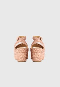 Talons plateformes tissés roses avec un design à lanières croisées, boucle réglable à la cheville et un talon en coin texturé.