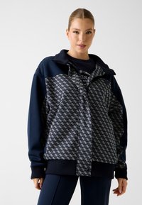 Marineblauwe pulloverjas met patroon op het voorpand, ritssluiting en geribbelde boorden. Voorzien van een kraag en details in contrasterende kleuren.