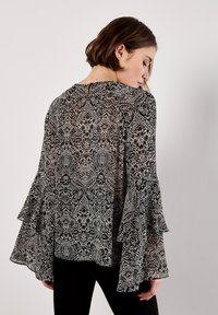 Zwart-wit gestreepte blouse met lange, uitlopende mouwen, voorzien van een sleutelgatdetail op de rug en een doorschijnende, gestructureerde stof.