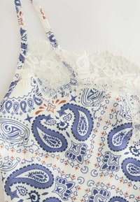 Strap dress with blue and orange paisley print and white floral lace trim along the neckline on a light background.