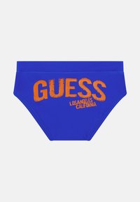 Kék úszónadrág sima anyagból, élénk narancssárga "GUESS" és "LOS ANGELES CALIFORNIA" felirattal az elején.