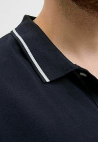 Marineblaues Poloshirt mit strukturiertem Stoff und einem weißen Akzentstreifen entlang des Kragens. Nahaufnahme, die die Details des Kragens hervorhebt.
