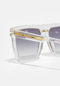 Ochelari de soare din plastic transparent cu lentile gri degradate; au accente aurii pe brațe. Formă rectangulară cu un design îndrăzneț.