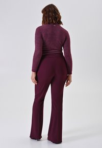 Mauve gebreide trui met aansluitende silhoët en lange mouwen, gecombineerd met bordeauxrode flare-broek. Glad textuur, minimale details.