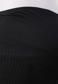 Svarta åtsittande leggings med en ribbad textur på den nedre delen och en slät midjeresår. Materialet verkar elastiskt och mjukt.