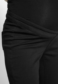 Calças de maternidade pretas com uma cinta elástica, apresentando um tecido suave, detalhes de costura subtis e um corte ajustado.