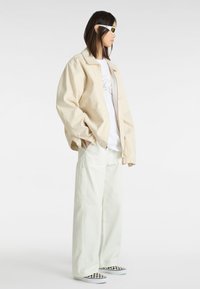 Creme oversized jakke over en hvid grafisk t-shirt, parret med mintgrønne vide bukser og sort-hvide ternede slip-on sko.
