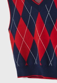 Mouwloos breivest met een rood en marineblauw ruitpatroon en witte diagonale lijnen, met een ribbelrand en V-hals.