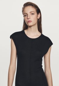 Czarny dopasowany top z krótkimi, wygodnymi rękawkami, okrągłym dekoltem i gładką fakturą, zaprojektowany z minimalnym wykończeniem szwów.