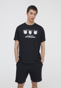 T-shirt nera in cotone a maniche corte, con una grafica di tre sveglie e il testo "risveglio senza fine" in bianco.