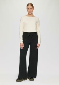 Crème lange mouwen top met een brede halslijn, gecombineerd met zwarte broek met elastiek en brede pijpen van een gestructureerde stof, gedragen met chunky zwarte schoenen.