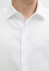 Witte overhemdd met een visgraatpatroon, een button-down kraag en kleine knopen. De stof heeft een gladde textuur en een getailleerde pasvorm.