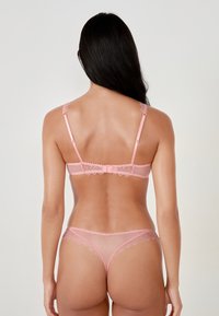 Roze kanten lingerieset met een doorschijnende beha van gestippeld stof en golvende randen, en een bijpassende slip met soortgelijke details.