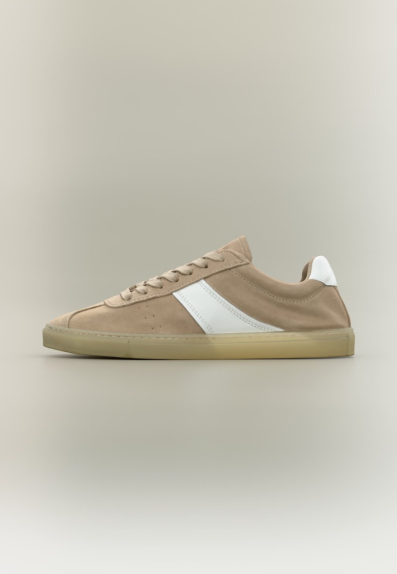 Baskets basses en daim beige avec bande diagonale blanche, languette blanche au talon, lacets beige et semelle en caoutchouc beige translucide sur fond neutre.