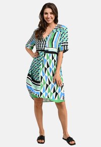 Kurzarmkleid mit geometrischen Mustern in Grün, Blau und Schwarz. V-Ausschnitt-Design mit lockerer Passform, das über das Knie reicht.