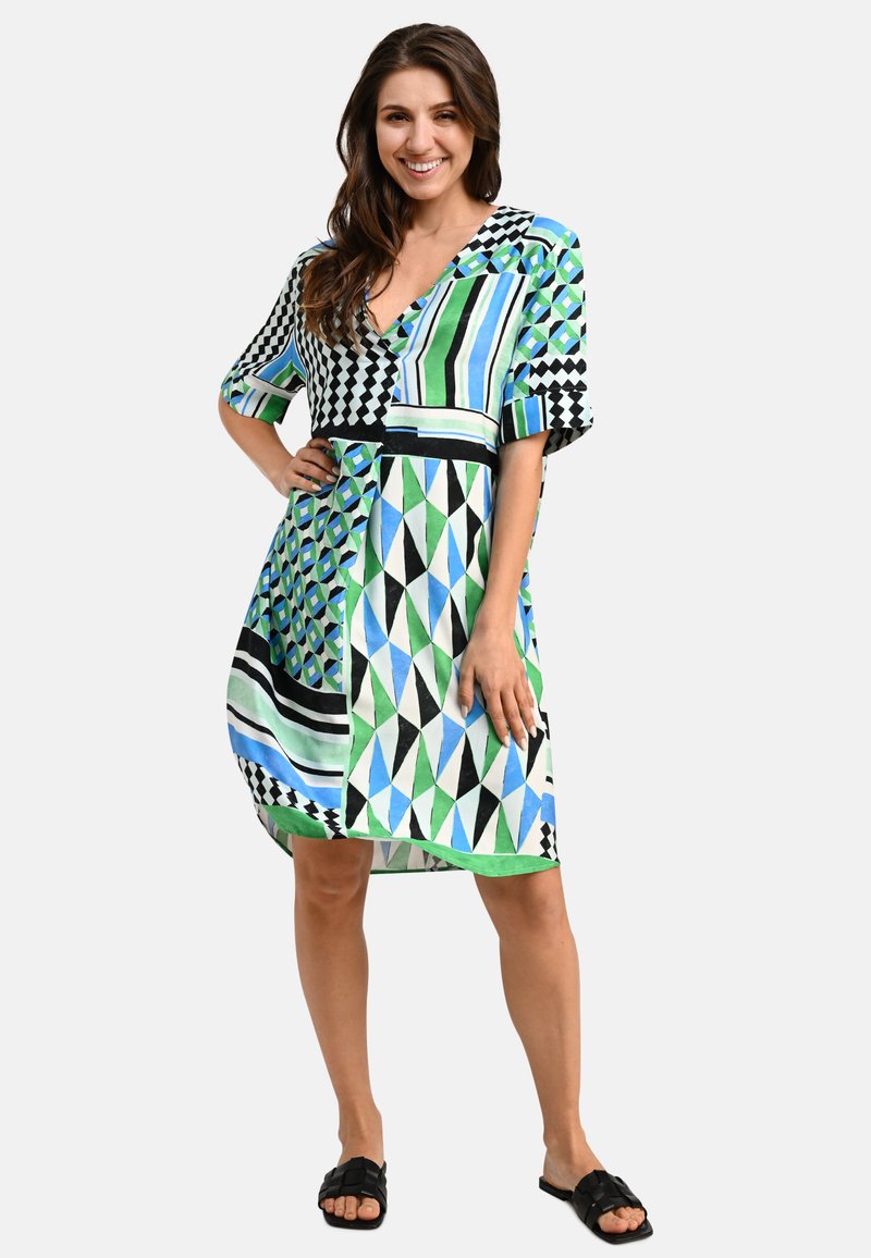 Kurzarmkleid mit geometrischen Mustern in Grün, Blau und Schwarz. V-Ausschnitt-Design mit lockerer Passform, das über das Knie reicht.