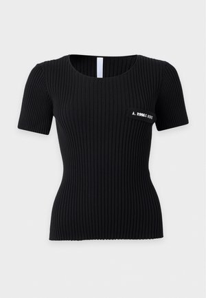 Femme portant un haut côtelé noir à manches courtes avec un texte sur la poitrine et un jean gris large taille haute avec des bottes noires à talons.