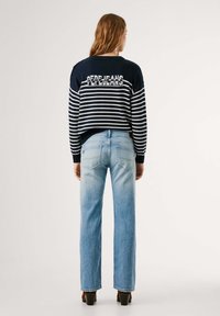 Zilā un baltā svītrainā adītā džempera ar "PEPE JEANS" tekstu aizmugurē, kombinēts ar gaiši ziliem taisnais kājām džinsiem un brūnajām papēžkurpēm.